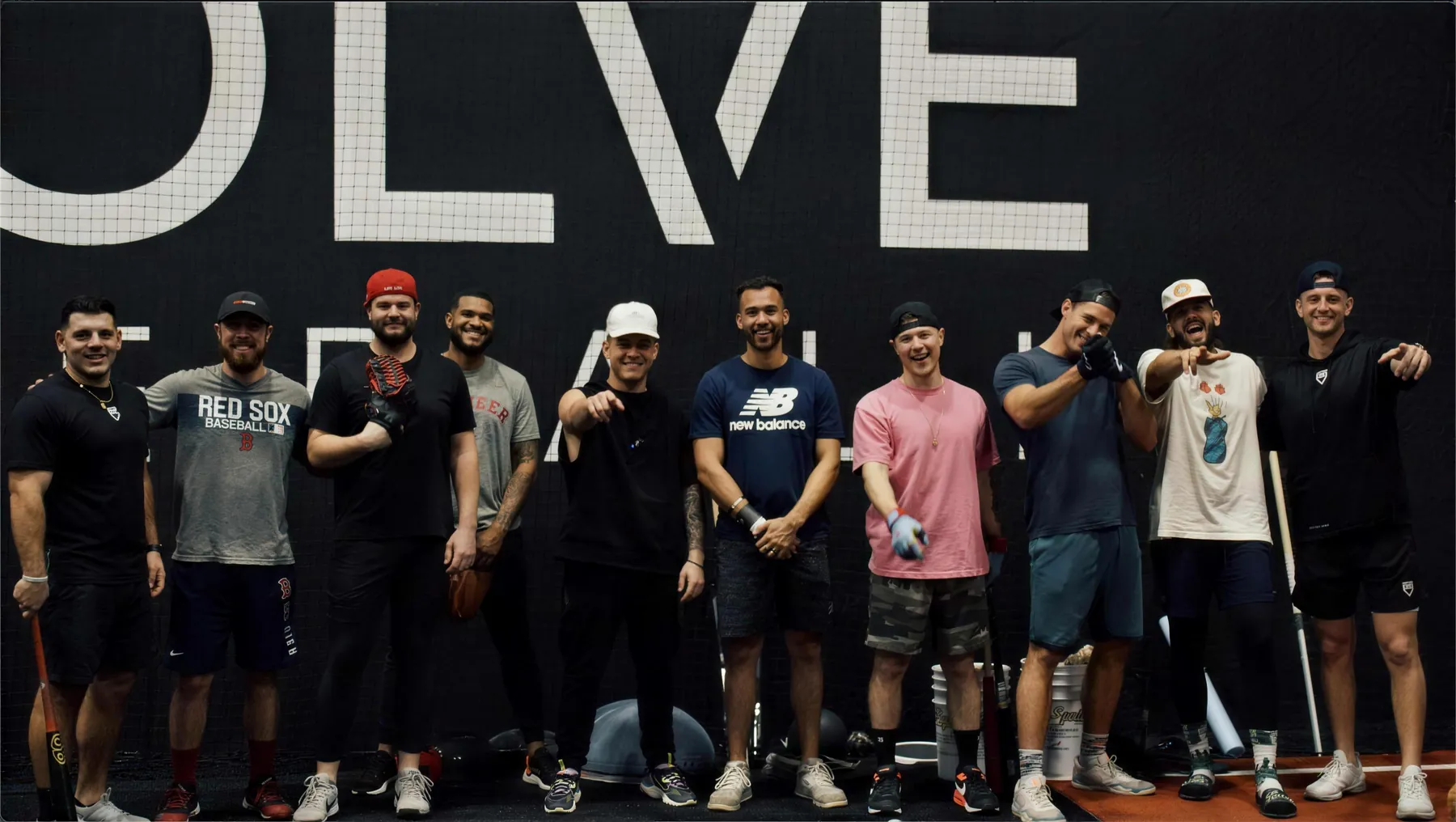 The Evolve Baseball coaching staff and players in front of the facility wall logo